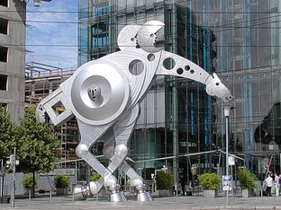 Eine große pferdeartige Statue welche zwei Halbmonde auf dem Rücken trägt. Im Hintergrund sind große moderne Gebäude sichtbar.