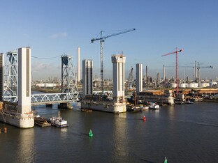 Eine große Brücke, die an einem Hafen steht. Boote und das Meer sind sichtbar, sowie Kräne im Hintergrund.