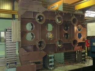 Große industrielle Zerspanungsmaschine in einer Fertigungshalle, bearbeitet Metallplatten mit kreisförmigen Aussparungen.