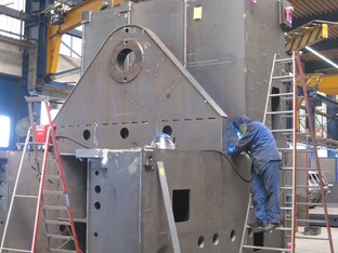 Ein Mann ist mit dem Schweissen einer großen Metallstruktur beschäftigt, während er verschiedene Werkzeuge verwendet.