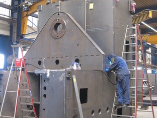 Ein Mann ist mit dem Schweissen einer großen Metallstruktur beschäftigt, während er verschiedene Werkzeuge verwendet.