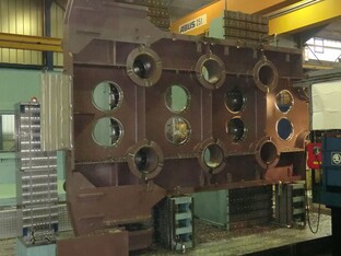 Große industrielle Zerspanungsmaschine in einer Fertigungshalle, bearbeitet Metallplatten mit kreisförmigen Aussparungen.